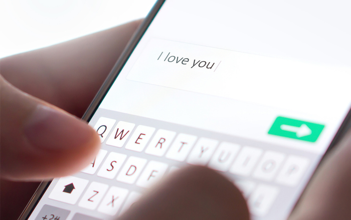 Sending I love you text message with mobile phone. Online dating, texting or catfishing concept. Romance fraud, scam or deceit with smartphone. Man writing comment.