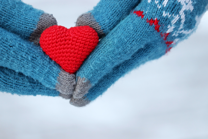 Concept of romantic love, winter weather. Hands in gloves holding a knit heart.