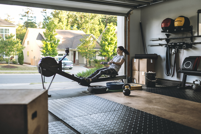 Active woman exercising on a rowing machine in her home garage gym during covid-19 pandemic.