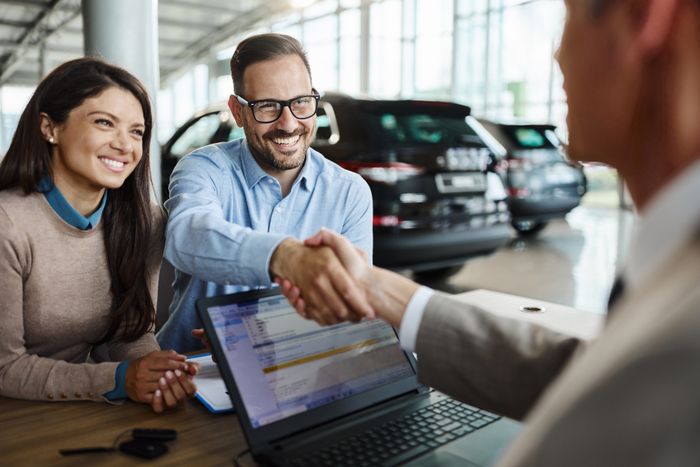 Happy couple came to an agreement with car salesperson in a showroom.