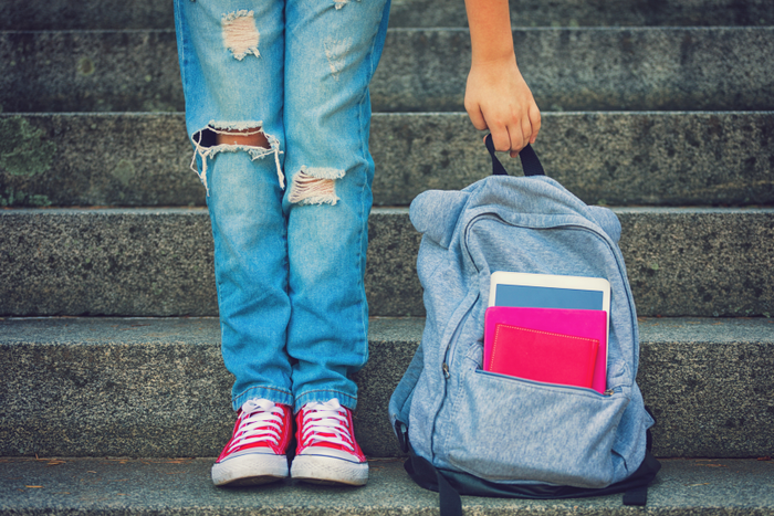 backpack with school folders and a child standing next to it with pink shoes
