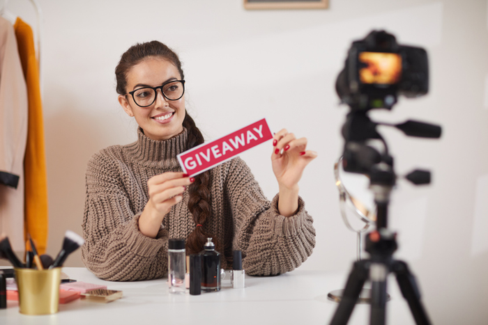 woman holding up sign saying giveaway in front of camera