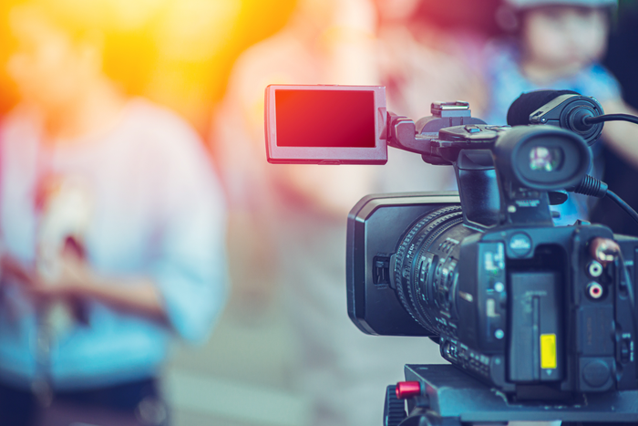 Video camera operator focuses on a blurred subject in the background.