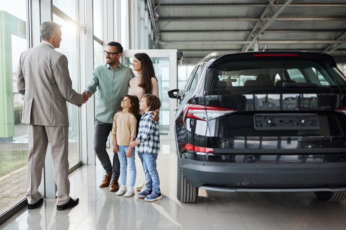 Young happy family shaking hands with a car salesperson in a showroom.