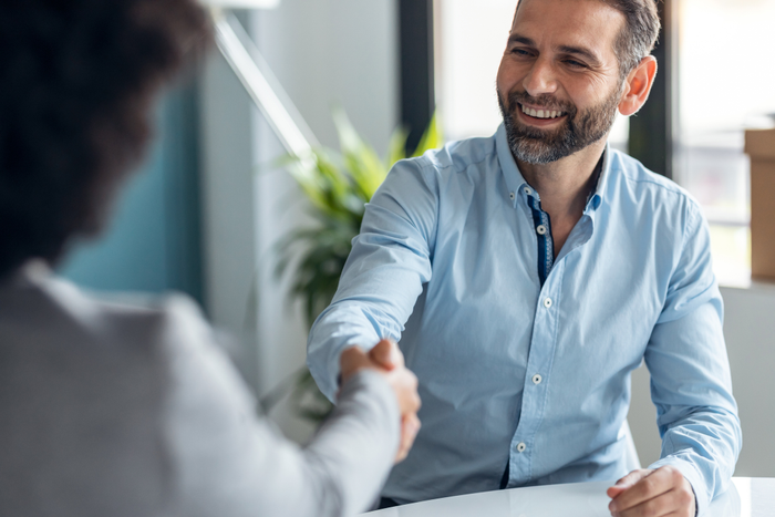 Attractive real-estate agent shaking hands with young couple after signing agreement contract in the office.