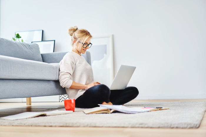 Female student sitting on floor of her apartment with laptop and notes 