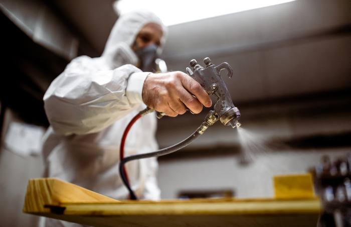 Carpenter painting wood with spray gun