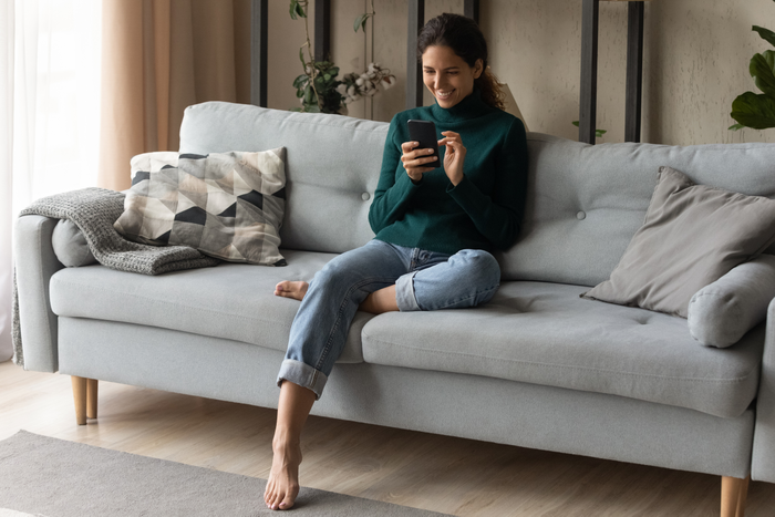 false Full length smiling young woman using phone, relaxing on couch