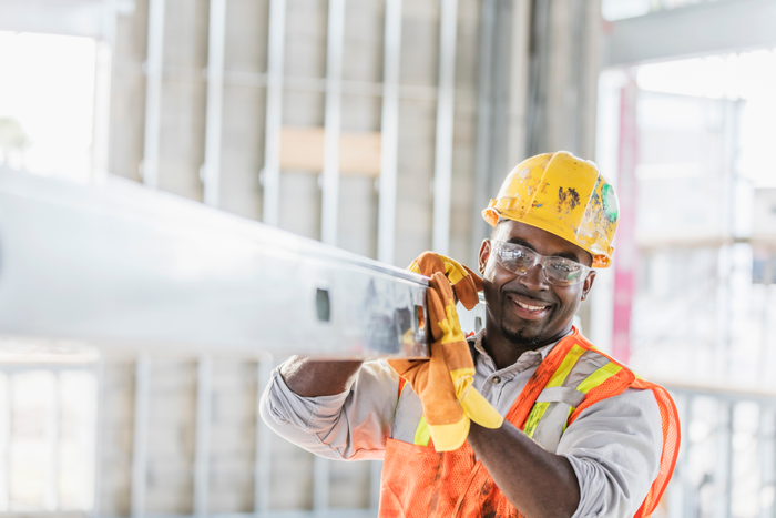 African-American construction worker carrying metal beam
