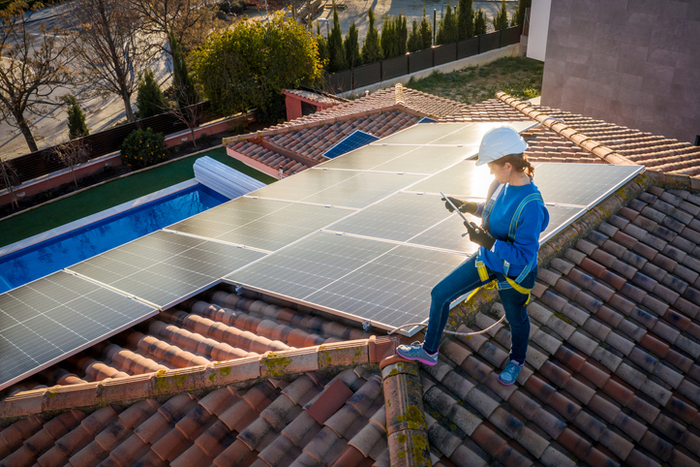 Technician woman working on maintenance of solar photovoltaic panel installed on domestic home rooftop with a tablet at sunset