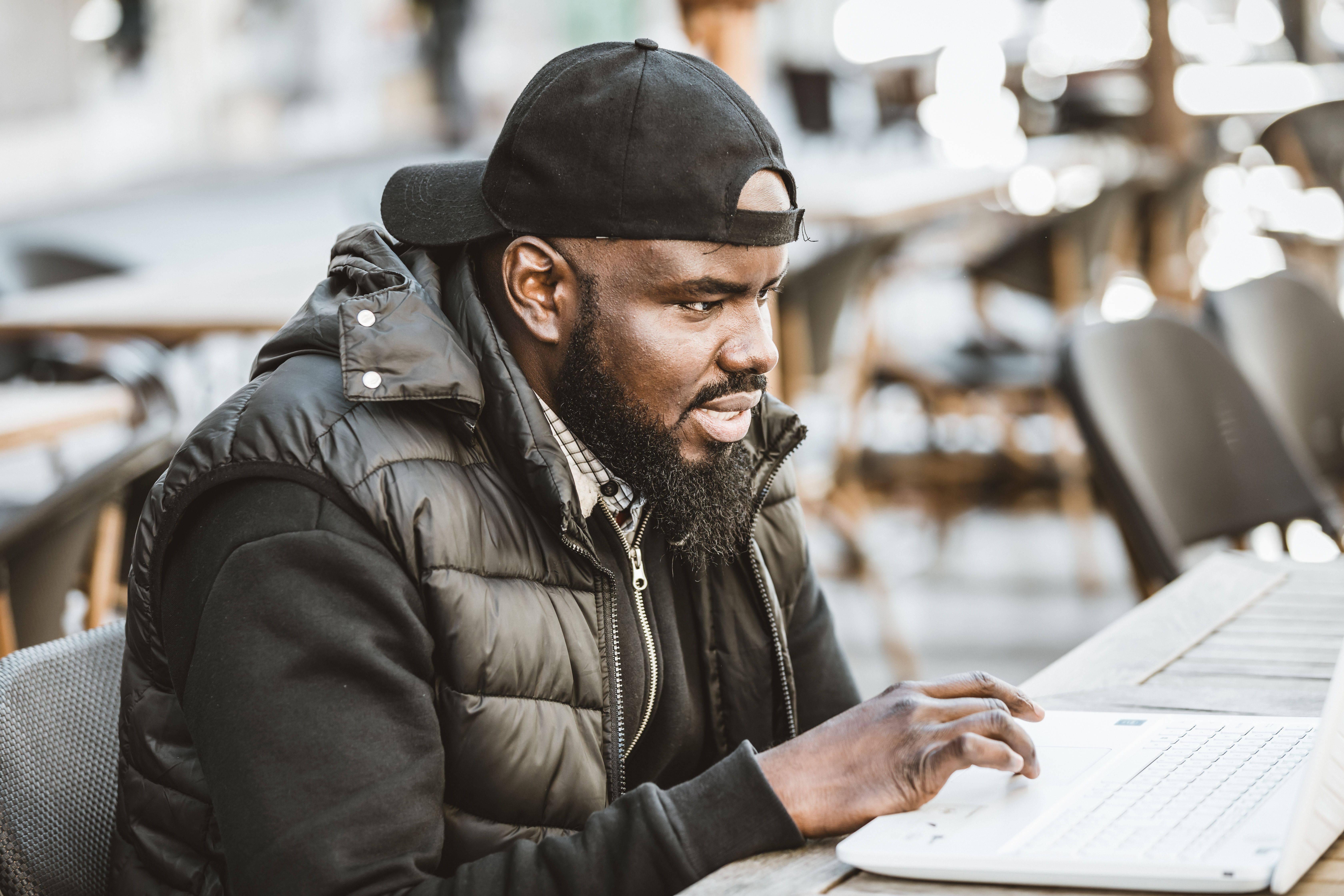 Happy black guy sitting at outdoor cafe with laptop computer
