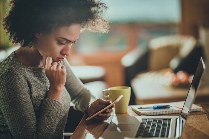 Women does research on phone while sitting at desk.