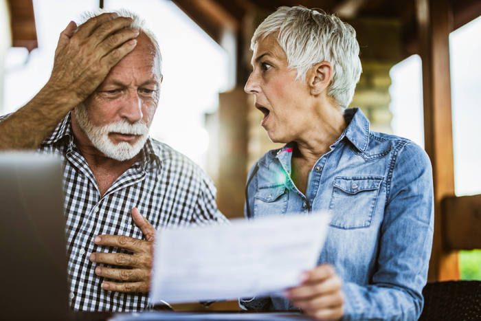 Shocked senior couple reading about scams in disbelief on their balcony.