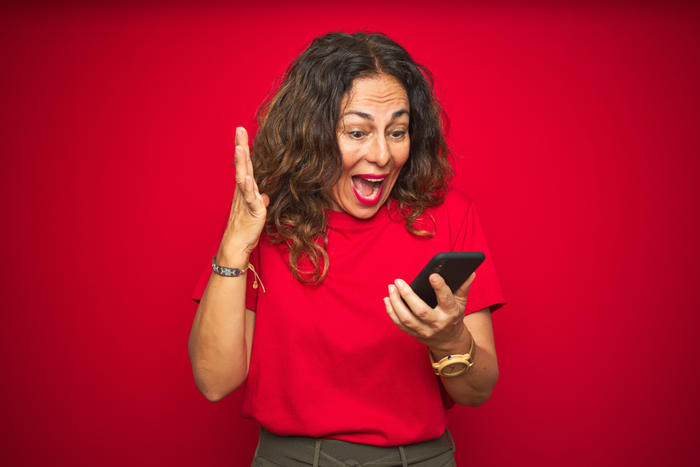 woman in red against a red background excitedly looking at her phone