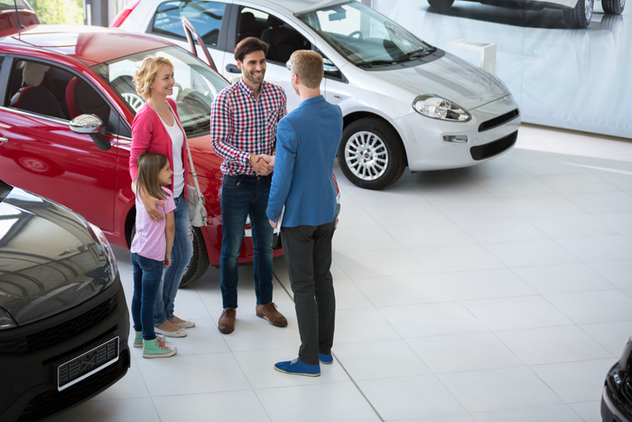 Car salesman shakes hands with a father to congratulate him and his family on buying a car