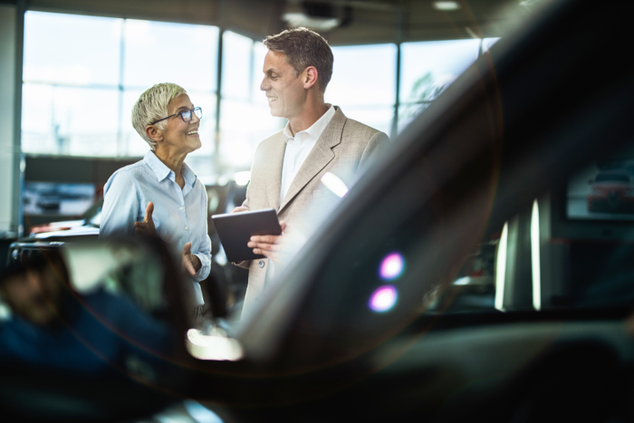 Happy car salesperson talking to senior businesswoman in a showroom.