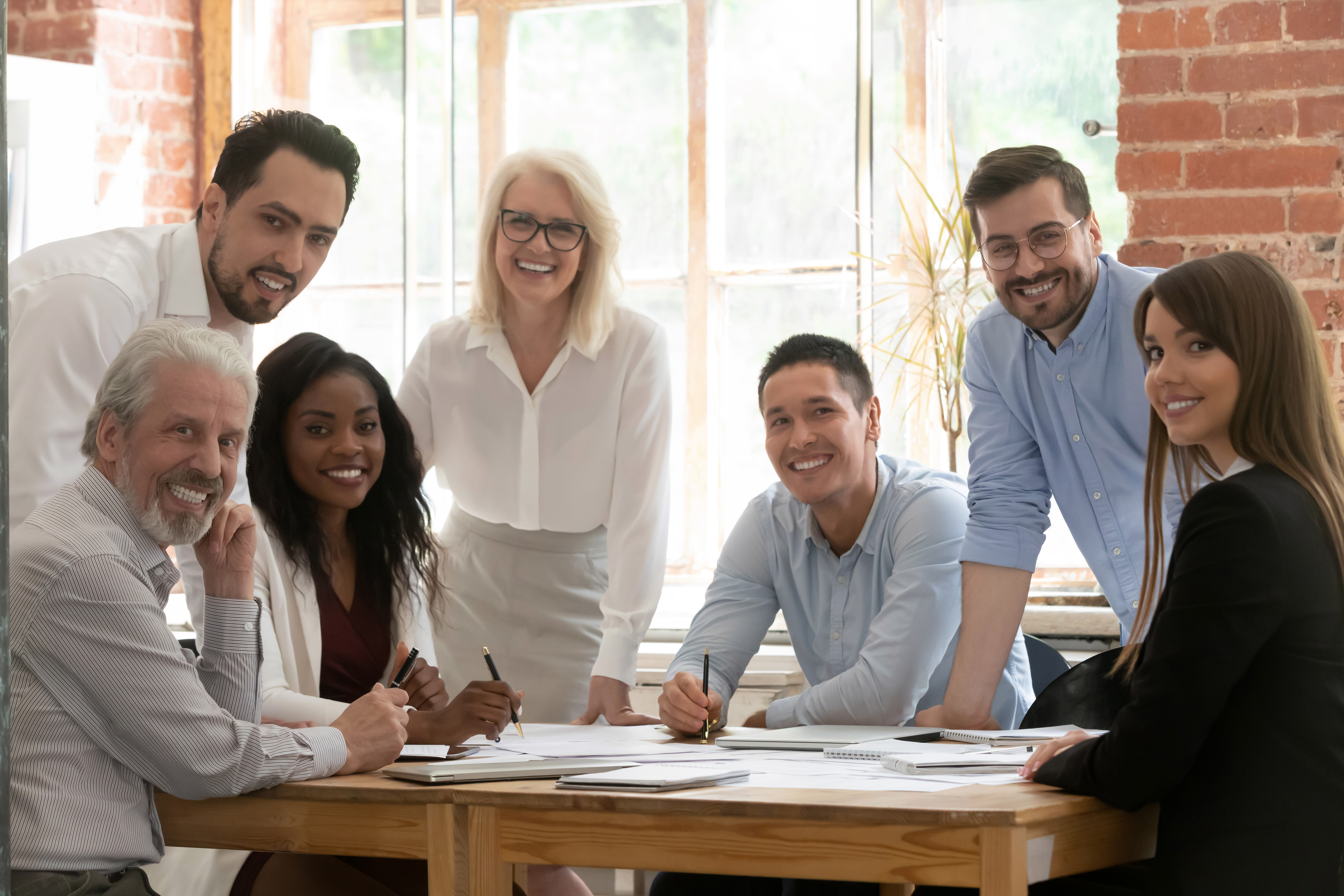 Professional business team young and old people posing together at office table, happy diverse leaders employees looking at camera, smiling multiracial staff corporate people workers group portrait