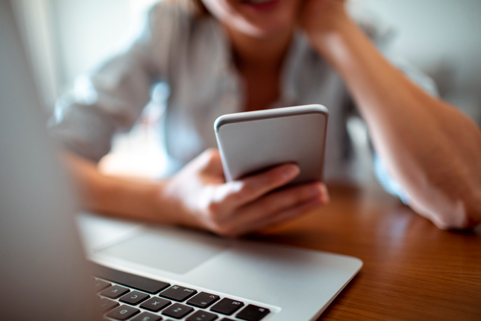 woman holding phone using laptop