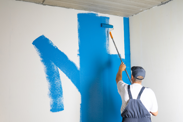Male painter painting a white wall with a roller in blue color renovations or construction concept.