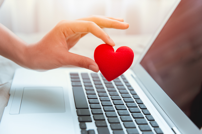Girl hand take red heart at laptop keyboard for social online love chat and sharing encouragement over internet to fight Covid-19 virus together.