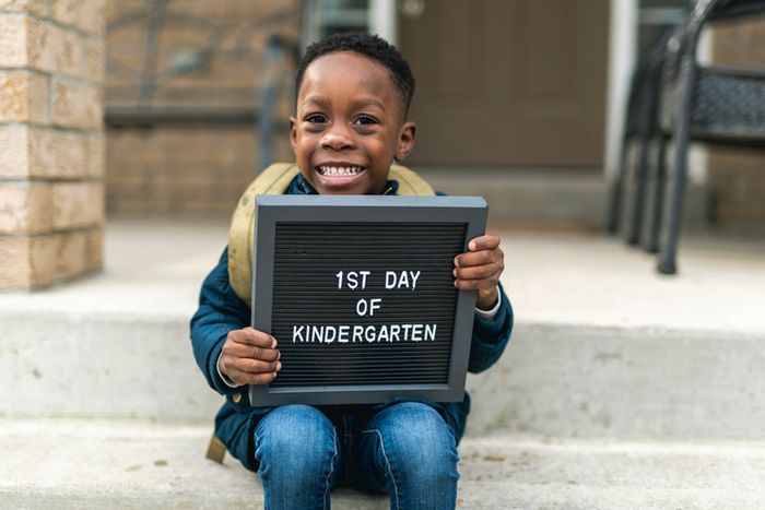 A cute boy holding up a first day of kindergarten sign