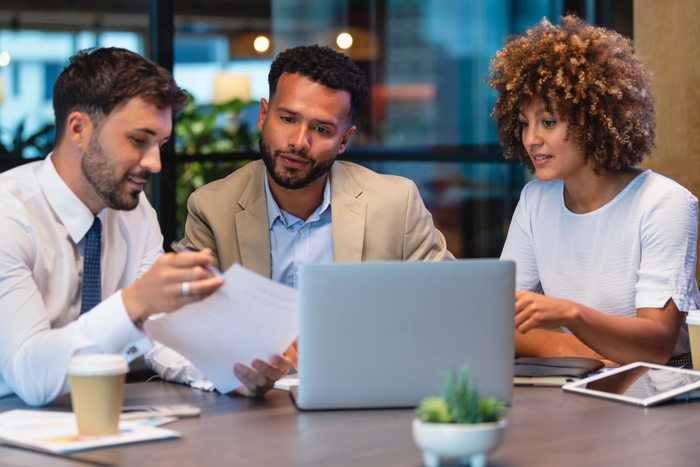 Three business people meeting and looking at a laptop and a document.