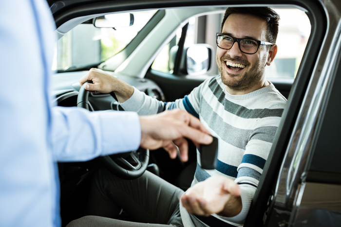 Young happy man receiving new car keys in a showroom.