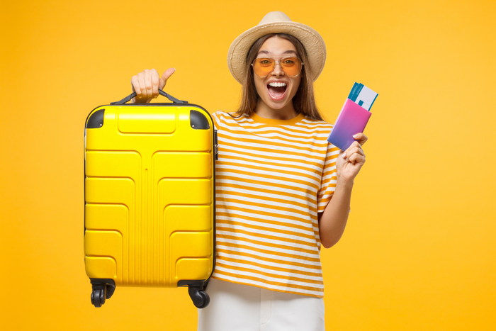 Woman with suitcase and airplane tickets isolated on yellow background excited about trip