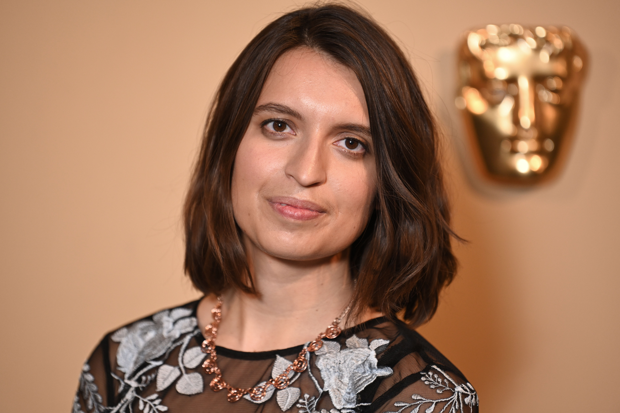 Adrienne Law. A woman with a shoulder length dark-brown bob wearing a black mesh top with embroidered flowers on it.