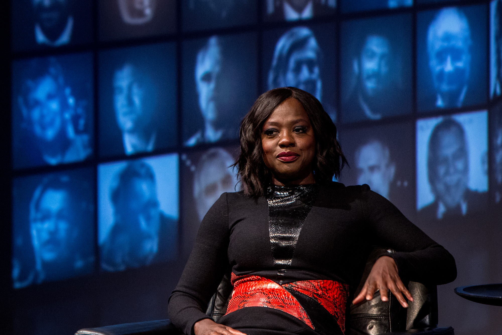 Viola Davis. A black woman with black bobbed hair wearing a black top with red statement belt.