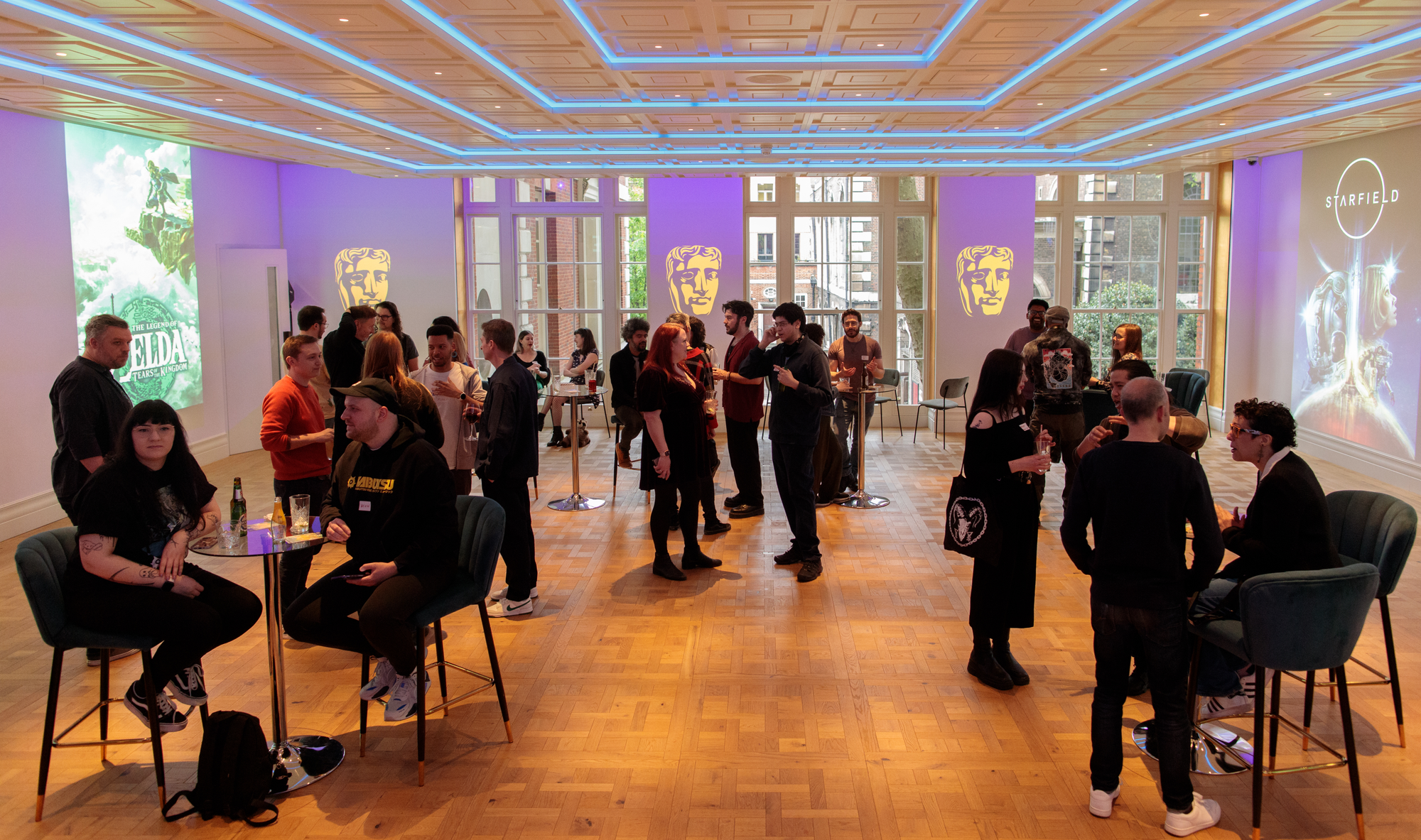 Groups of people chatting and networking in a large room with projections of the BAFTA mask on the walls.